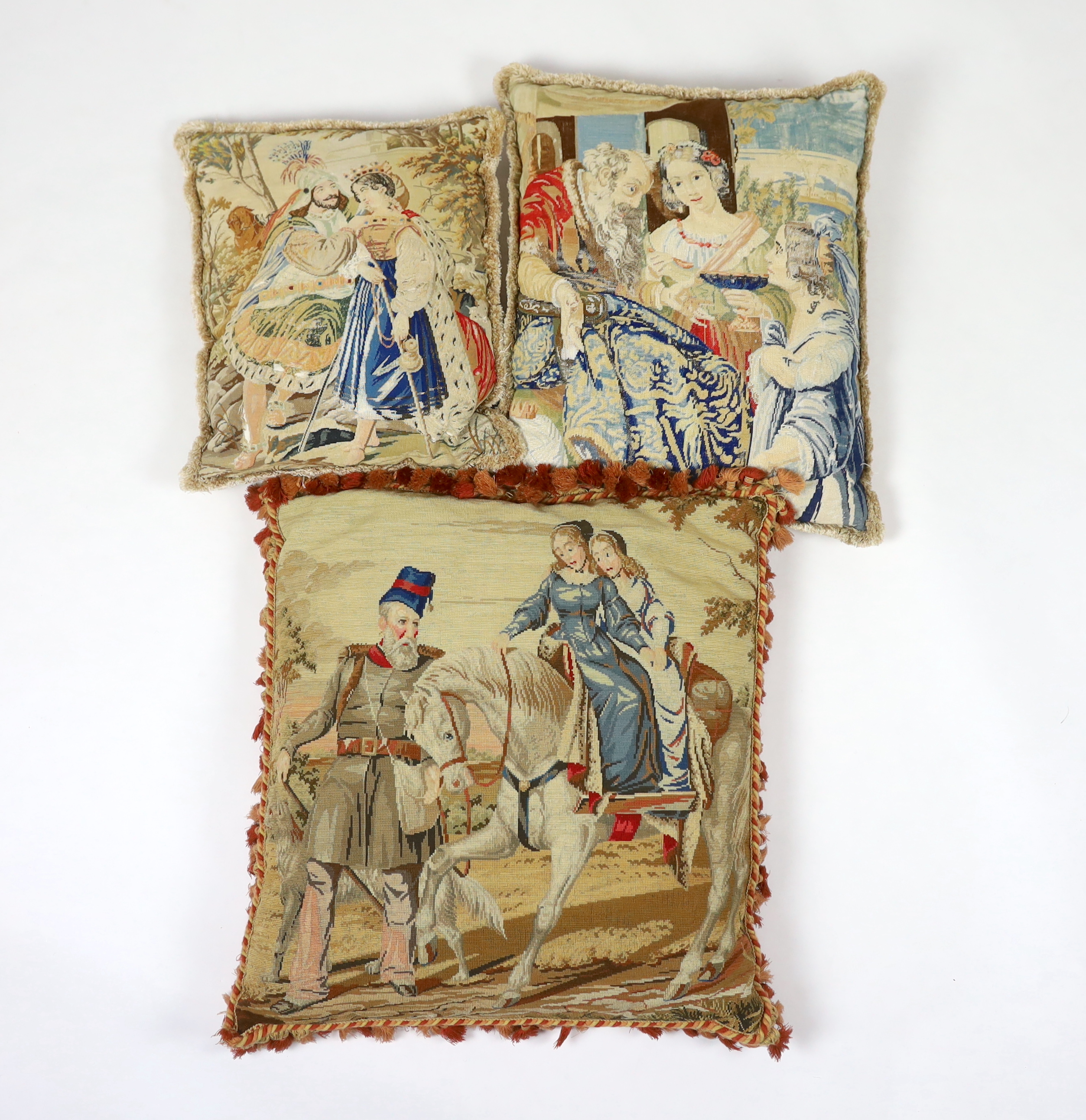 A very large Victorian Berlin wool worked cushion of possibly Queen Victoria's daughters on horseback being led by a gentleman in uniform, the cushion is edged with red tasselling, together with two similar Victorian Ber